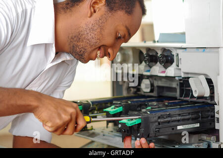 L'uomo sporgendoti fotocopiatore aperto durante la manutenzione le riparazioni utilizzando lo strumento palmare, nero parti meccaniche Foto Stock