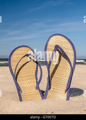 Coppia di paglia flip-flop bloccato in spiaggia di sabbia oltre il cielo blu Foto Stock