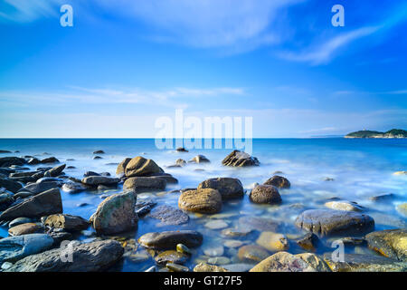 Baratti bay, rocce in un oceano blu sotto un cielo chiaro sul tramonto. Toscana, Italia. Foto Stock