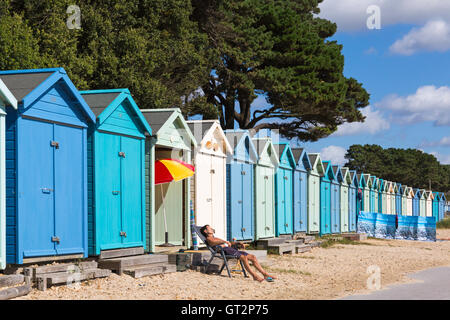 Donna anziana che prende il sole presso le capanne sulla spiaggia in una calda giornata di sole ad Avon Beach, Mudeford, Christchurch, Dorset nel mese di settembre Foto Stock