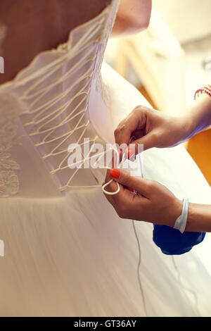 Closeup tonica foto di bella sposa di vincolare il suo abito da sposa Foto Stock