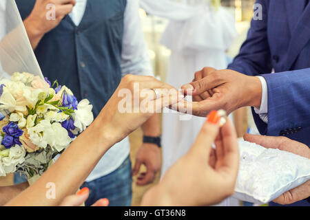 Le mani con anelli Groom mettendo golden ring sul dito della sposa Foto Stock