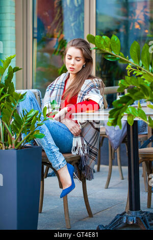 Giovane bella bruna ragazza siede in estate cafe in strada coperta avvolto Foto Stock