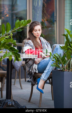 Giovane bella bruna ragazza siede in estate cafe in strada coperta avvolto Foto Stock