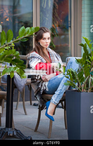 Giovane bella bruna ragazza siede in estate cafe in strada coperta avvolto Foto Stock