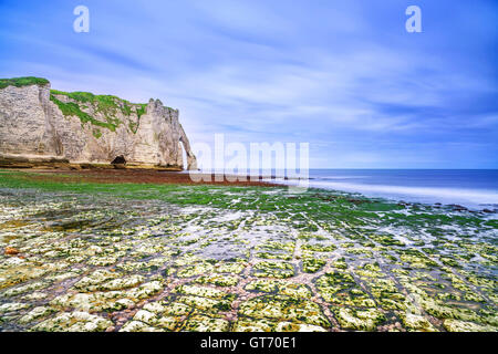 Etretat Aval cliff punto di riferimento e la sua spiaggia di bassa marea sotto un cielo nuvoloso. La Normandia, Francia, Europa. Lunga esposizione. Foto Stock