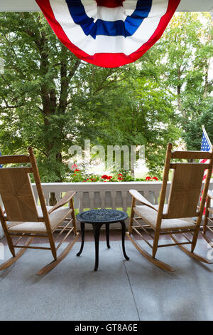 Legno di due sedie a dondolo con piccolo tavolo presso la terrazza con concettuale bandiera americana dirige anche alti alberi verdi presso il giardino Foto Stock