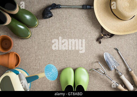 Bordo o cornice di utensili da giardinaggio su una posizione neutra di beige background tessile con giardino scarpe e stivali, cappello, annaffiatoio, mano Foto Stock