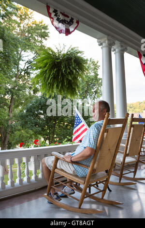 Felice Medioevo uomo seduto su legno sedia a dondolo in terrazza e la visualizzazione di una natura rilassante mentre godendo il quarto giorno o Foto Stock