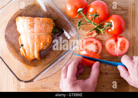 Lo chef prepara un gourmet cena di salmone fresco per affettare pomodori a grappolo per accompagnare il succulento filetto di pesce in vetro piatto da forno Foto Stock