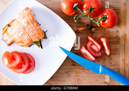 Deliziosi appena tostato di filetto di salmone fresco servito fresco con fette di pomodori a grappolo di essere preparati in una cucina con un moderno b Foto Stock