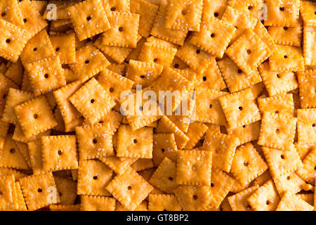 Texture di sfondo di quadri di formaggio crackers con fori centrali disposti in uno strato visualizzato close up full frame da sopra Foto Stock