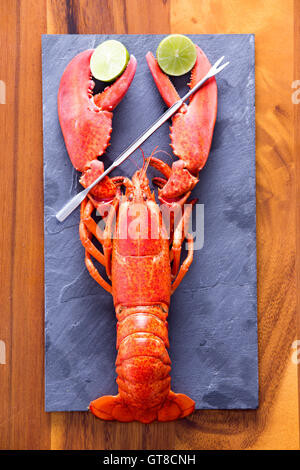 Close up Red Lobster ritaglio di fettine di lime sul grigio di un tagliere con grimaldelli, servita sulla parte superiore di una tavola di legno. Foto Stock