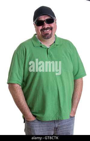 Ritratto di sovrappeso uomo che indossa camicia verde, cappellino da baseball e occhiali da sole in piedi in studio con le mani nelle tasche dei jeans, Foto Stock