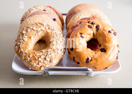 Chiudere fino deliziosi bagel cotti al forno pane per Office snack impilati su un vassoio di bianco e servite in tavola. Foto Stock