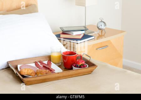Rilassante colazione a letto con caffè, frutti di bosco freschi, cornetti e la pancetta e un tempo per leggere con una pila di libri assortiti su Foto Stock