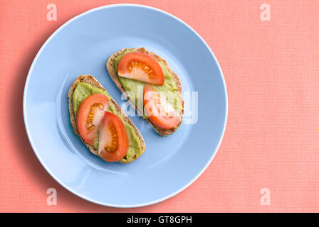 Vista superiore della piastra blu con sani e avocado sandwich di pomodoro su rosa sullo sfondo di stoffa Foto Stock