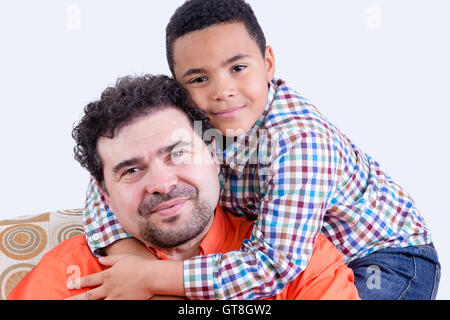 Allegro bambino in maglia a scacchi con grin abbraccia il suo padre sorridente con la barba da dietro Foto Stock