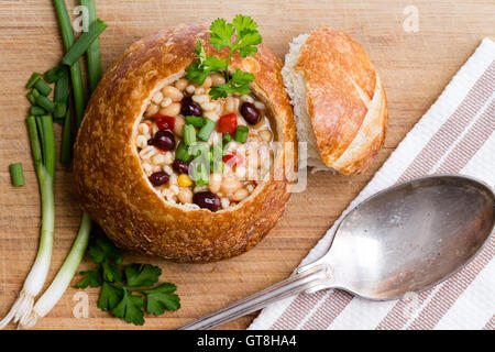 Vista superiore del delizioso pane ciotola con fagioli, orzo e verdure accanto a pezzi di cipolla verde e il coriandolo e cucchiaio Foto Stock