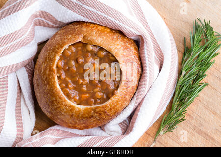 Cucinata fresca pane caldo ciotola di zuppa di lenticchie avvolto nel panno assorbente accanto a rametti di rosmarino su tavola Foto Stock