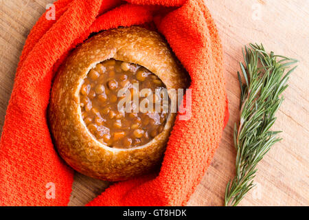 Cucinata fresca pane caldo ciotola di zuppa di lenticchie avvolto nel panno rosso igienico accanto a rametti di rosmarino su tavola Foto Stock