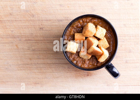 Unico che serve della deliziosa zuppa di lenticchie guarnito con crostini tostati nella coppetta con manico sul tavolo di legno Foto Stock