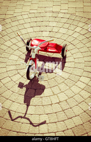 Elevato angolo di visione della Red Vintage triciclo sotto il sole in getto forte ombra sul Patio pietre disposte in configurazione circolare ou Foto Stock
