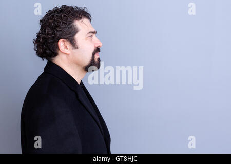 Profilo di calma bello dai capelli scuri e barbuto uomo di mezza età che indossa la maglia nera e blazer su sfondo grigio con copia s Foto Stock
