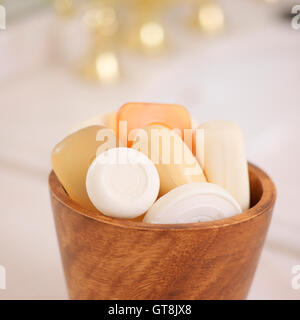Varietà di barre di sapone in ciotola di legno con oro rubinetto di lavello in background Foto Stock