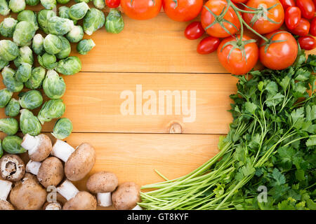 Confine sani di verdure fresche per la cottura su una tavola di legno con i cavoli di Bruxelles, i pomodori, il prezzemolo e baby bella mushroo Foto Stock