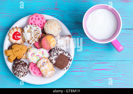 Piastra di colore bianco pieno di cioccolato zuccherini, fragola, pan di zenzero e altri cookie aromatizzato accanto al rosa tazza di latte oltre crackled Foto Stock