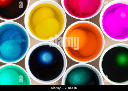 Tintura di hard-boiled uova di galline per la Pasqua con un vicino la vista aerea del bianco fresco uova la macerazione in singoli vasi di colorante Foto Stock