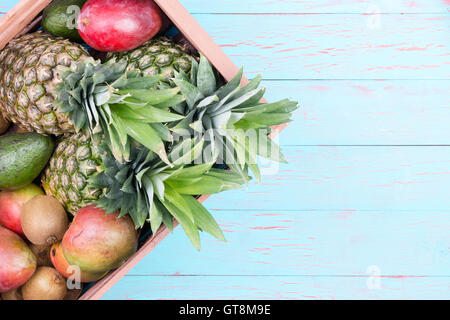 Rettangolare di scatola di cartone degli ananassi, manghi, avocadi e kiwi su tavole di legno in blu con spazio di copia Foto Stock