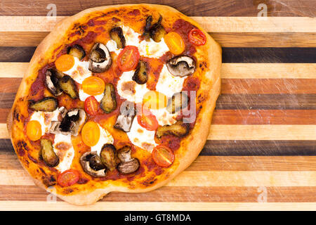 Unico fatto a mano pizza al formaggio con i funghi e le fette di pomodoro su strisce di legno tagliere Foto Stock