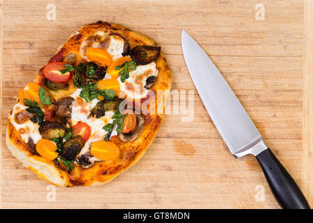 Appena sfornati si lancia a mano pizza vegetariana con funghi, pomodoro e mozzarella su un tagliere di legno a fianco di un ki Foto Stock