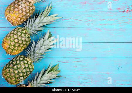 Fila di quattro inclinate ananas frutta stabilite sul blu vecchi pavimenti in legno o tavolo con spazio di copia Foto Stock