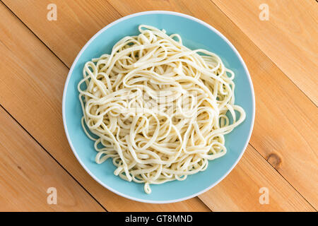 Di placcato recentemente bollita plain spaghetti servita su una piastra blu su una tavola di legno Tavolo da giardino con diagonale di plance, vista aerea Foto Stock