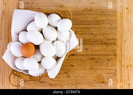 Unico riempito di vimini con singolo uovo marrone sulla parte superiore di quelli bianchi su un tavolo di legno con uno sfondo con spazio di copia Foto Stock