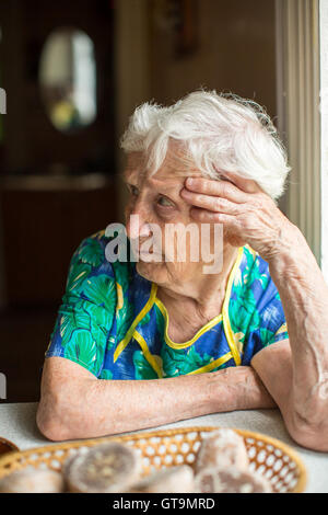 Anziani infelice donna seduta al tavolo. Foto Stock