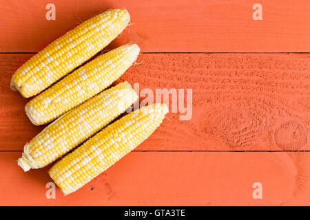 Quattro fresche dolci pannocchie di granoturco disposte in una fila come un lato sinistro bordo su un arancio tavolo in legno con copia spazio, vista aerea Foto Stock