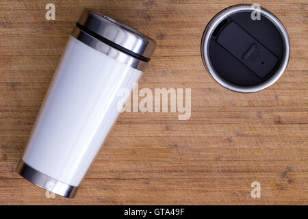 Vista dall'alto in basso sulla coppia di bianco in bianco e acciaio inox thermos che stabilisce e in piedi su marrone liscia superficie di legno con Foto Stock