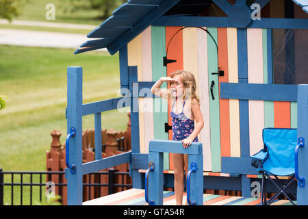 Carino bambina con la mano sopra gli occhi gridando a qualcuno di attività ricreative all'aperto playhouse con manubrio, la sedia, la porta e il vento Foto Stock