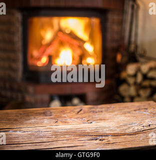 Vecchio tavolo in legno e camino con fuoco caldo sullo sfondo. Foto Stock