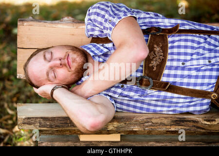 Giovane uomo in tradizionali abiti bavarese dormire sul banco di prova all'aperto Foto Stock