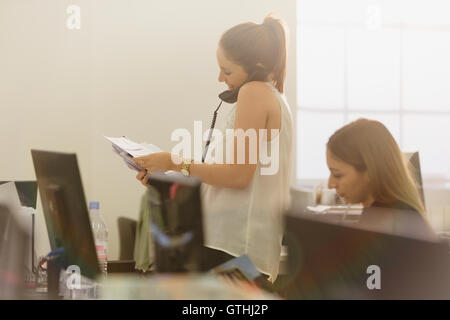 Imprenditrice con scartoffie parlando al telefono in ufficio Foto Stock