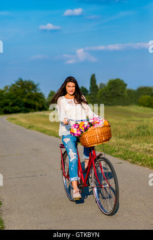 Giovane ragazza scorre una bicicletta con un cesto pieno di fiori Foto Stock