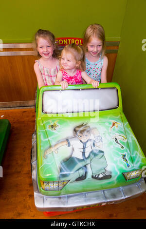 Tre ragazze di età compresa tra i 2 4 6 anni / giovani sorelle / bambini / Kids / ragazza godere a gettone bambino in auto in un centro commerciale per lo shopping arcade Foto Stock