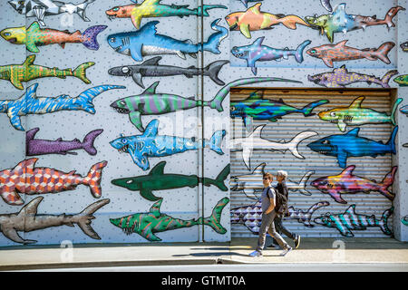 Due adulti passando davanti ad un dipinto murale di squalo a Wellington, Nuova Zelanda Foto Stock