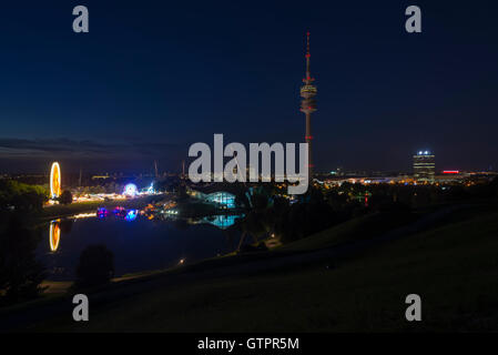 Panorama del Parco Olimpico di Monaco di Baviera con una fiera estiva al tramonto con illuminata Olympic Tower, BMW Welt, Allianz Arena Foto Stock