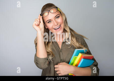 Ritratto di una bella gioiosa ragazza degli studenti tenendo in mano libri colorati, isolata su uno sfondo grigio, si torna a scuola Foto Stock